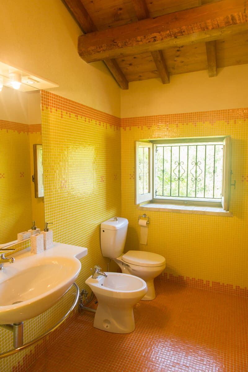 Bathroom with yellow and orange mosaic tiles and wooden beam ceiling