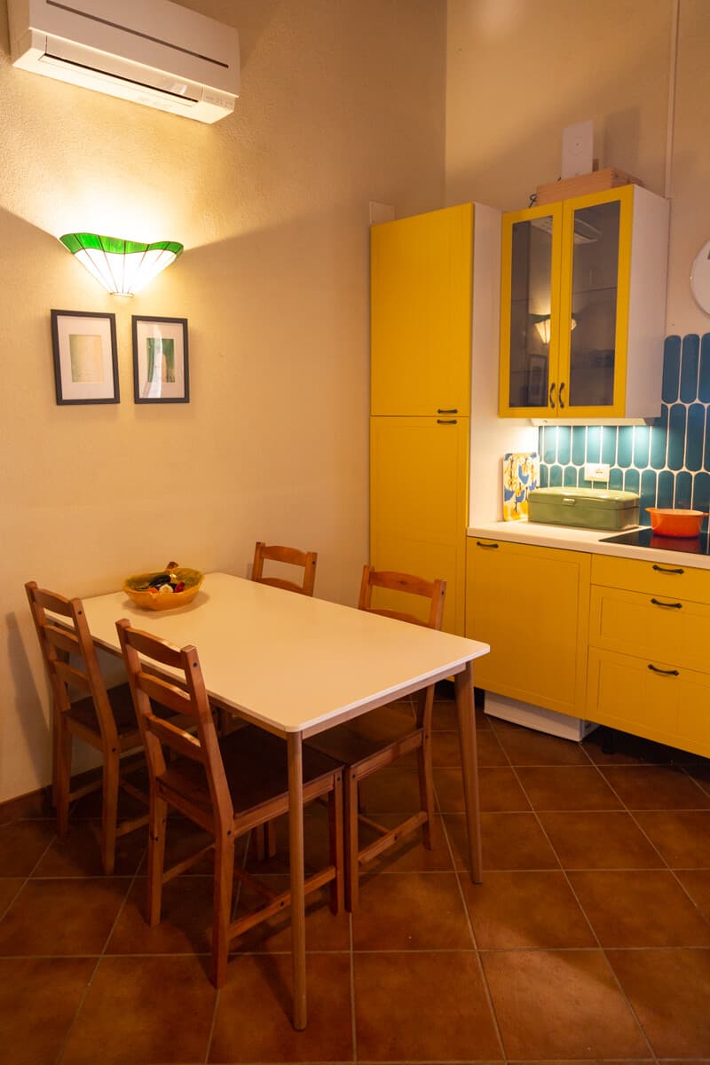 Dining table with wooden chairs next to yellow kitchen cabinets