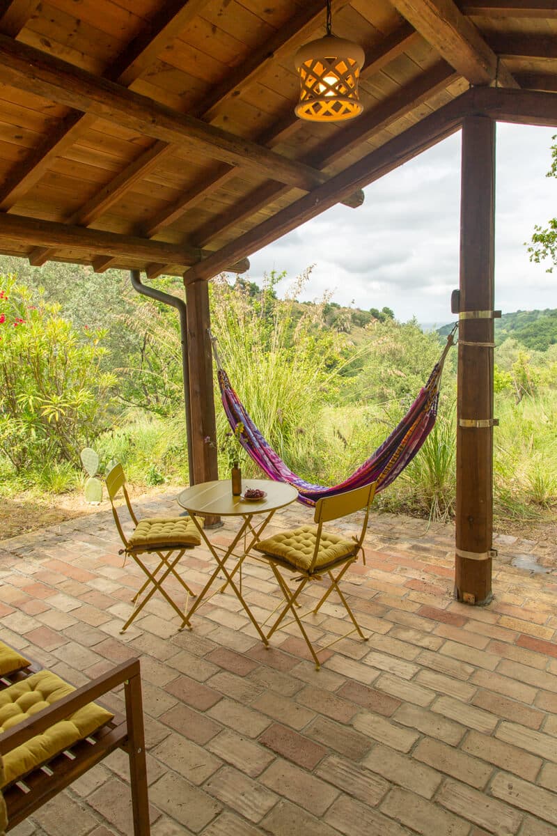 Covered stone patio with hammock, bistro table and chairs overlooking the garden